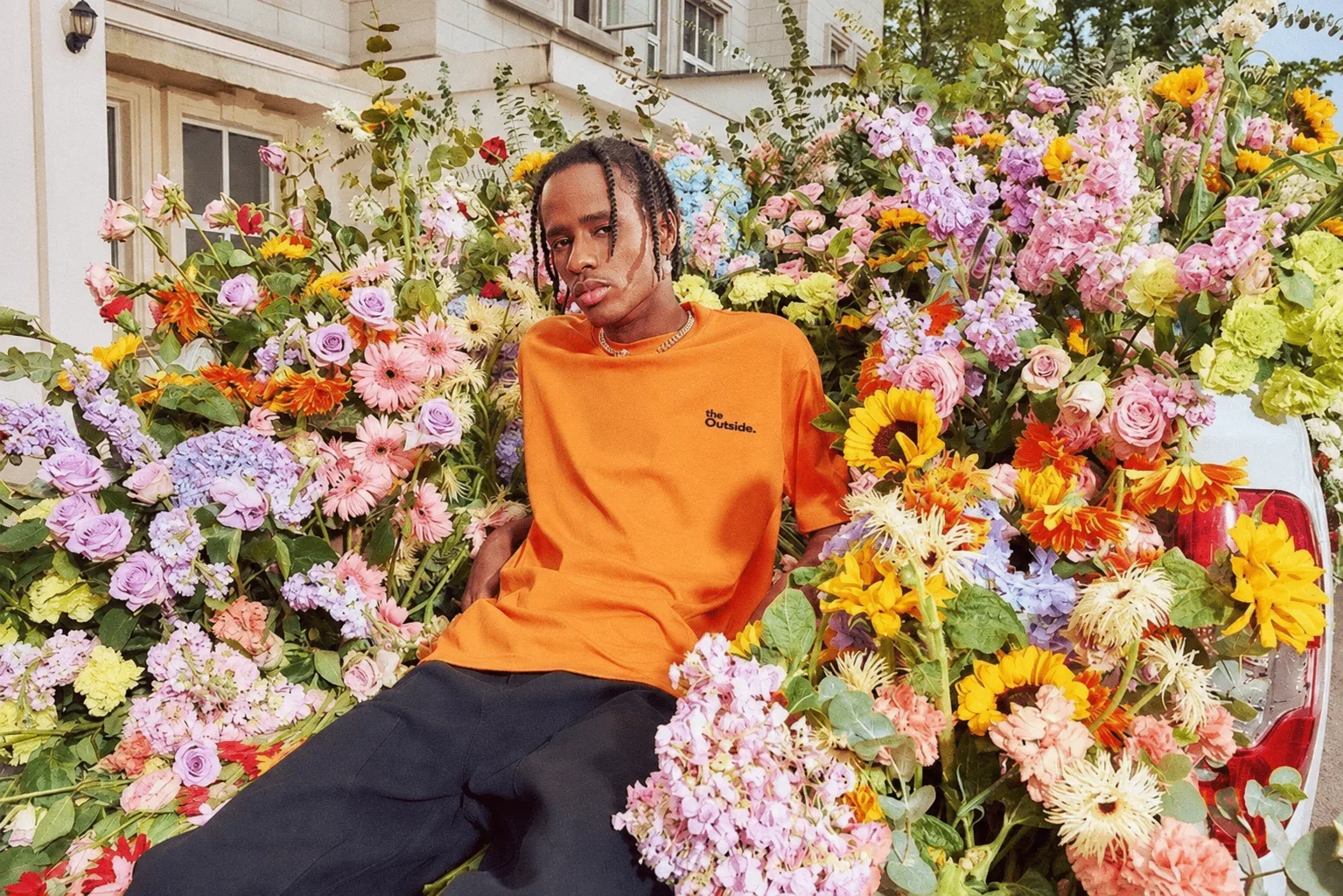 A person in an orange Theoutsideside tee surrounded by flowers